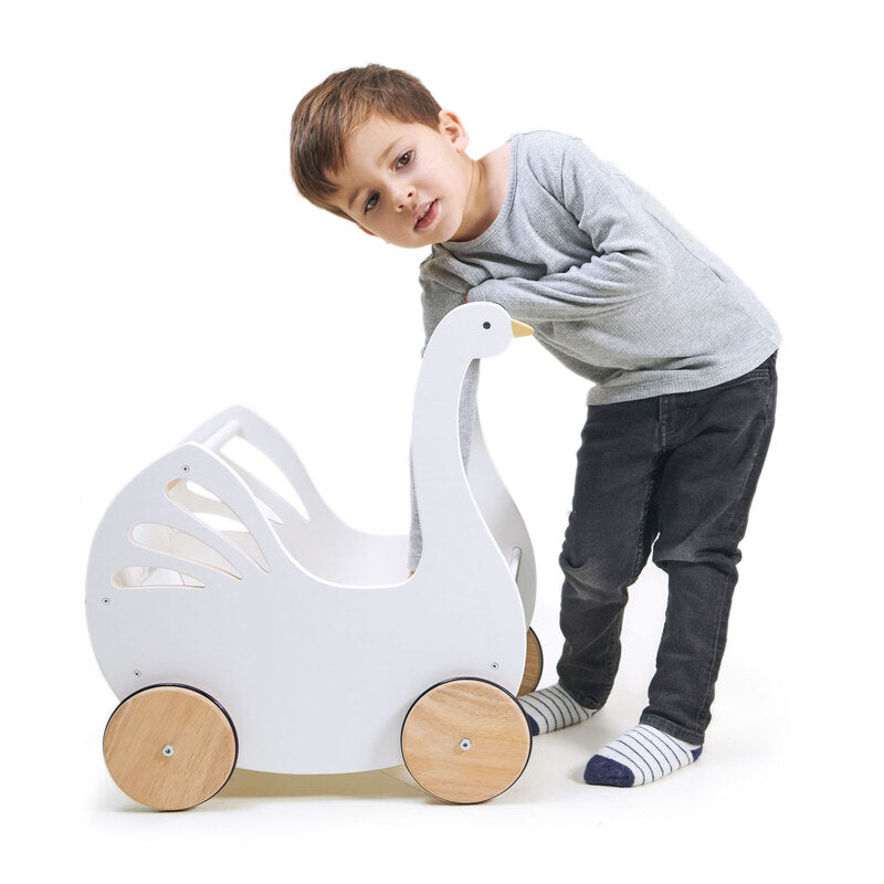 Young child leaning into a white wooden doll pram shaped like a swan, on a white background.