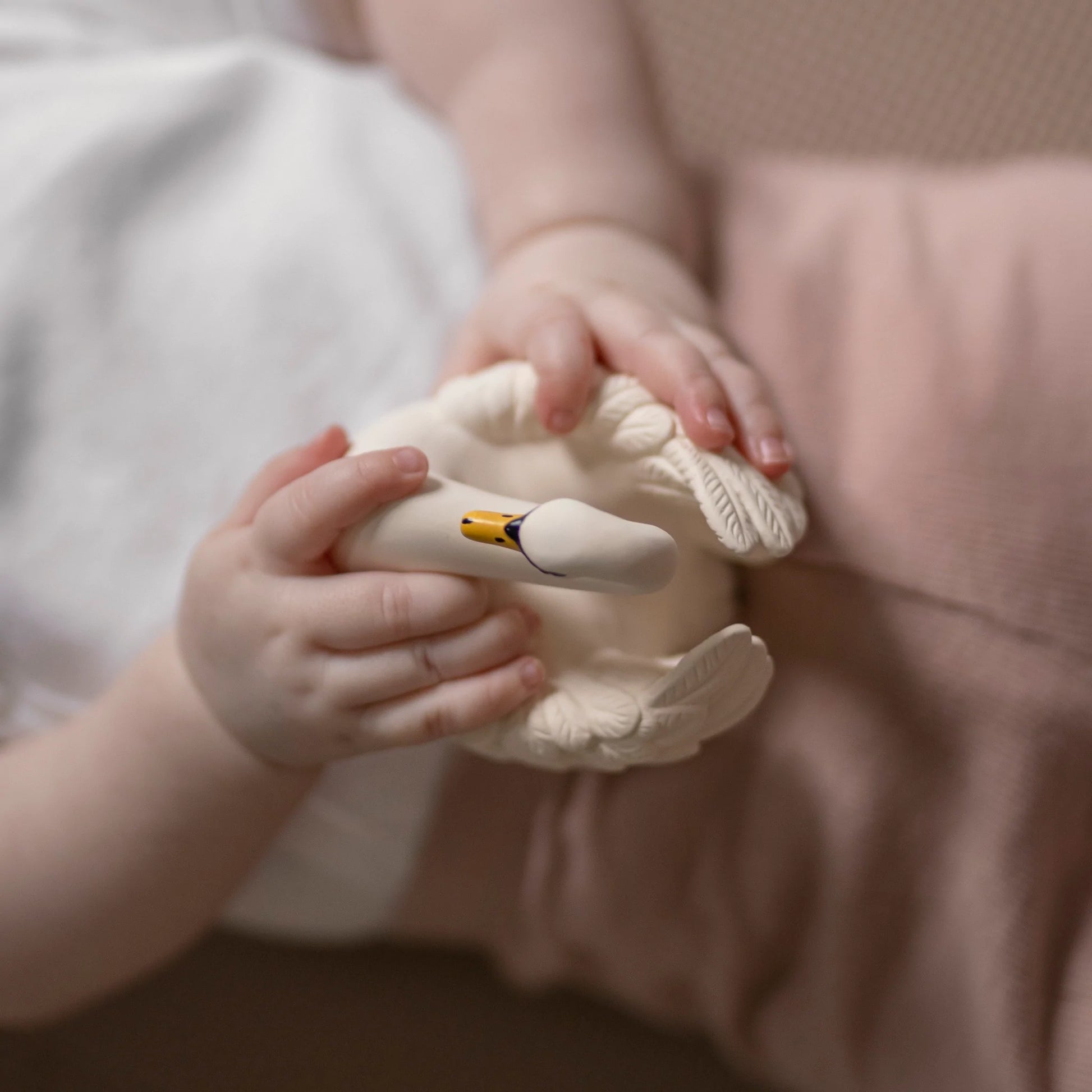 Baby's hands holding cream rubber swan shaped bath toy