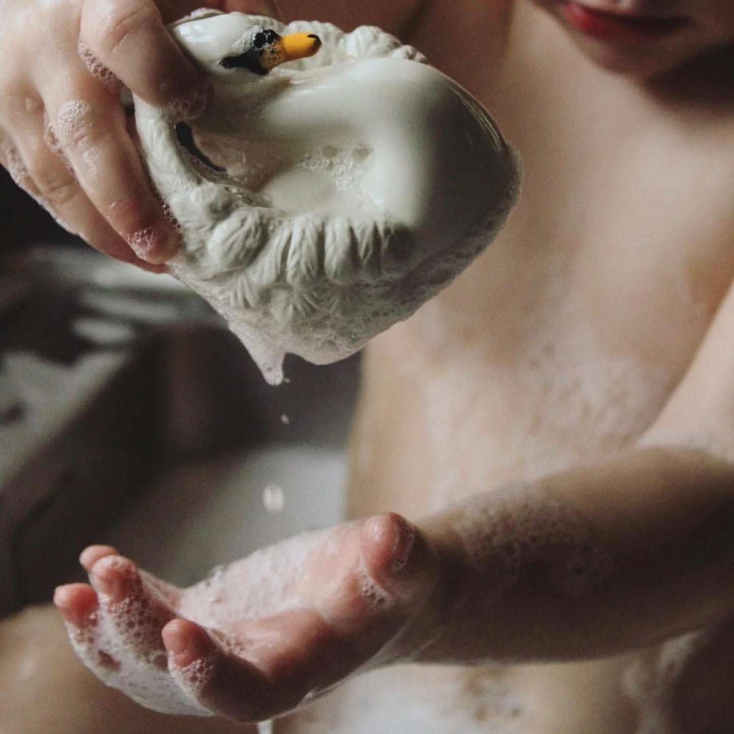 Young child holding cream rubber swan shaped bath toy, in bath with bubbles
