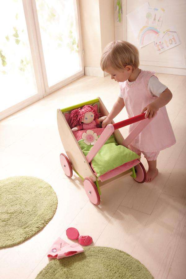 Young girl wearing pink dress playing with Haba Cherry Blossom wooden doll pram