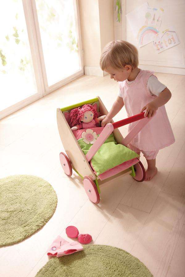 Young girl wearing pink dress playing with Haba Cherry Blossom wooden doll pram